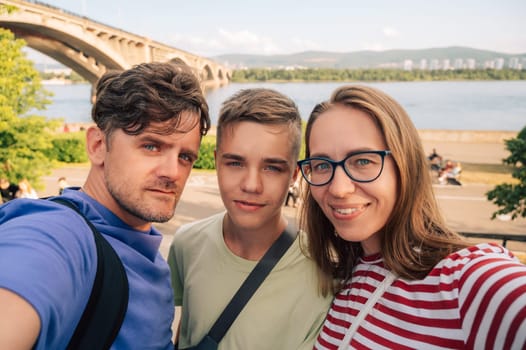 Happy family taking a photo on the Yenisei River background at beauty sunny summer day in Krasnoyarsk city.