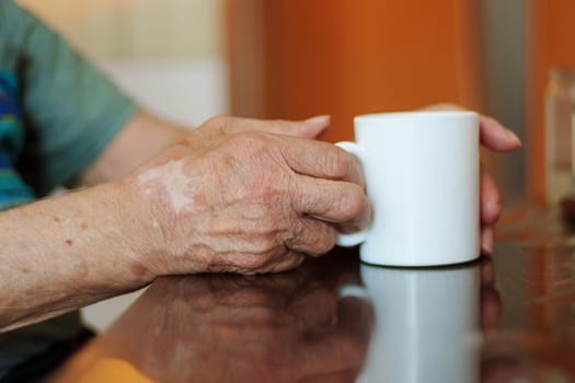 Elderly hands resting on a table beside a white mug in a warm indoor setting during a leisurely afternoon