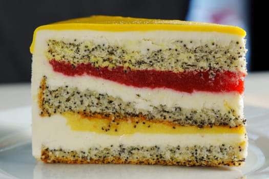 A stunning cross-section of a colorful layer cake featuring poppy seeds, cream, and vibrant fruit jelly on a sunny afternoon