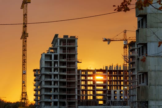 As the sun sets, a striking orange glow envelops the skyline, highlighting cranes and unfinished structures, showcasing the energy of urban development.