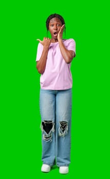 A young girl stands confidently pointing to the right against a bright green backdrop in studio