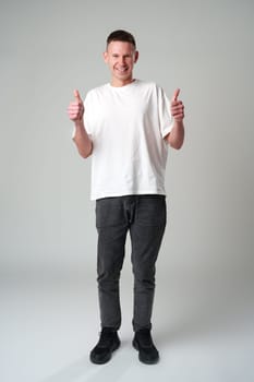Portrait of a cheerful young man showing okay gesture on gray background studio shot