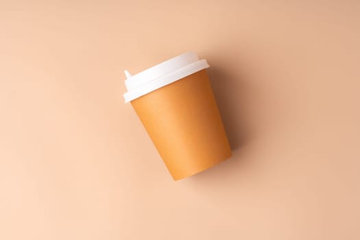 A simple disposable coffee cup on a warm beige background close up