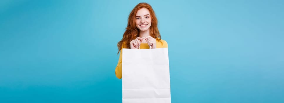 Shopping Concept - Close up Portrait young beautiful attractive redhair girl smiling looking at camera with white shopping bag. Blue Pastel Background. Copy space.