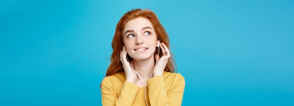 Lifestyle concept - Portrait of cheerful happy ginger red hair girl enjoy listening to music with headphones joyful smiling to camera. Isolated on Blue Pastel Background. Copy space