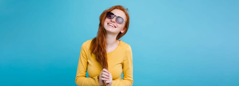 Portrait of happy ginger red hair girl with freckles smiling looking at camera. Pastel blue background. Copy Space.