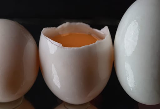 Three raw duck eggs are sitting in a row with an egg in the middle broken in half showing the yolk and white egg on dark background. use it as your Wallpaper, Poster and Space for text, Selective focus.