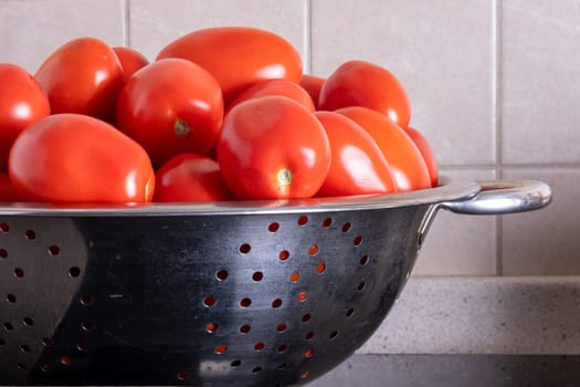 Ripe red tomatoes lying in a metal colander in the kitchen. Home canning. Selective focus.
