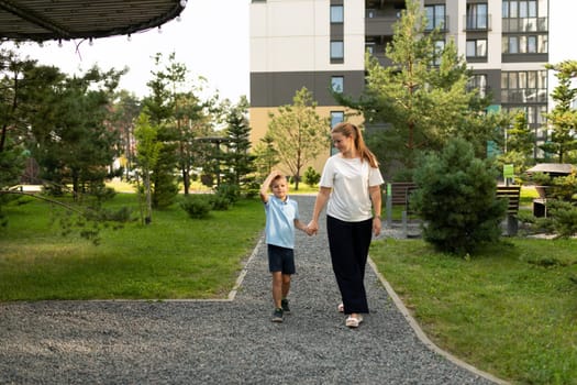 A mother and her son walk hand in hand through a vibrant park, surrounded by trees and greenery. Their joyful interaction reflects a deep and loving relationship.