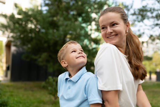 A mother and her young son share a warm and joyful moment in a sunny park. The boy looks up at her with a bright smile, radiating love and connection.