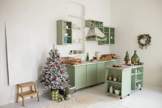 A cozy, bright kitchen decorated for Christmas with green cabinets, a small Christmas tree with decorations, and a festive table with snacks.