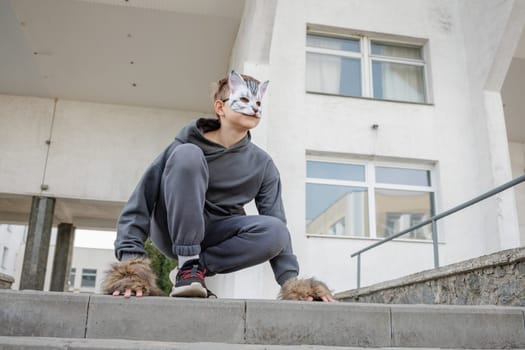 quadrobics teenager in cat mask sits on all fours in park, quadrobika subculture imitation of animal actions