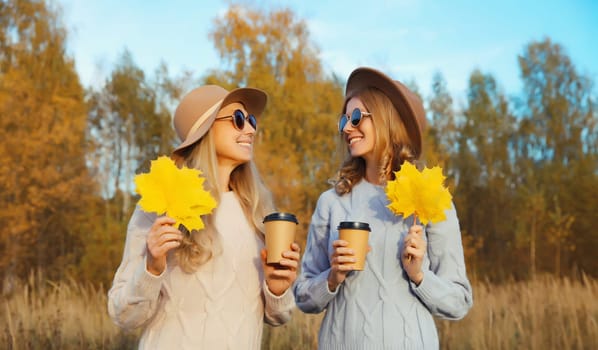 Portrait of happy young two women friends with autumn yellow leaves, stylish smiling girlfriends together outdoors, in sunny park, fall season