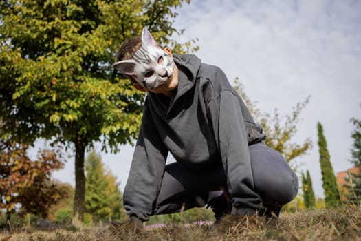 quadrobics teenager in cat mask sits on all fours in park, quadrobika subculture imitation of animal actions
