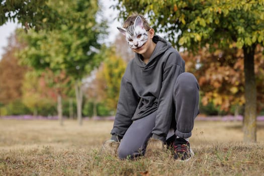 quadrobics teenager in cat mask sits on all fours in park, quadrobika subculture imitation of animal actions