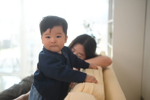 Cute toddler standing on sofa at home. Child development, parenting and family concept.