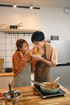 Happy young couple wearing aprons enjoying cooking together and sharing a meal in cozy kitchen.