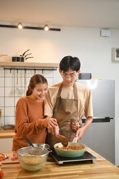 Happy young couple enjoying time together while preparing meal in a cozy kitchen.