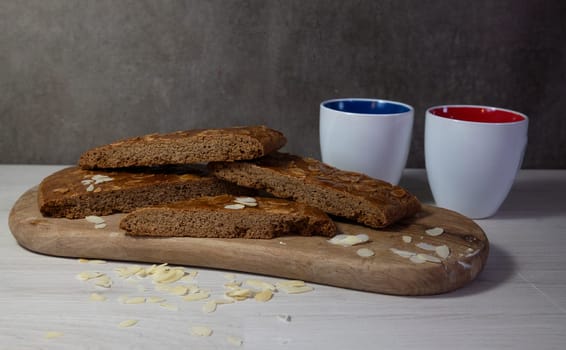 homemade speculaas cake, dSliced homemade almond biscotti displayed on a wooden board, accompanied by two colorful coffee mugs, creating a cozy and inviting atmosphere ideal for coffee breaks.
