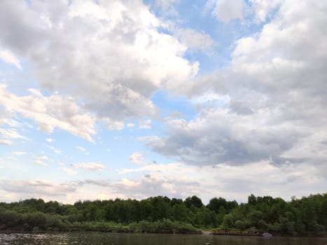 A serene river reflects the sky, surrounded by trees and greenery under a cloudy evening sky.