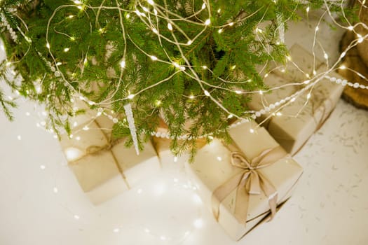Designer Christmas tree decoration with light decorations. The concept of celebrating New Year and Christmas. Gifts in craft packaging under the Christmas tree.