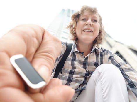 A middle-aged woman who is tourist and blogger takes selfies near skyscrapers in Hong Kong on a trip