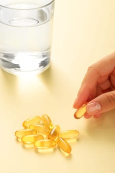 Hand picks up one omega-3 capsule from a handful of similar capsules.