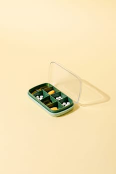Green plastic pill box with various pills and vitamins for every day, copy space.