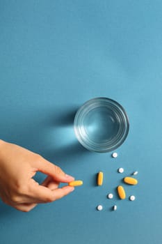 Hands with pills and a glass of water on a blue background. Perfect for healthcare and medical themes, copy space.