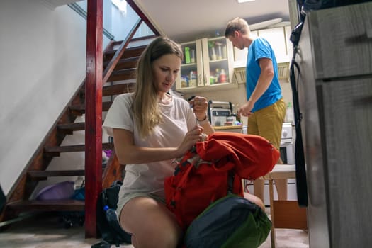 Two enthusiastic travelers are organizing their gear for an exciting outdoor journey in a cozy indoor setting