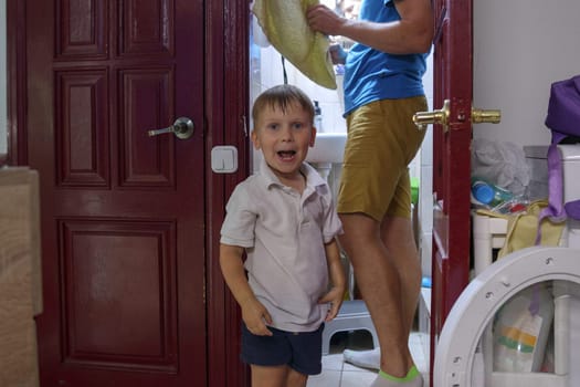 A joyful young boy grins playfully in a vibrant, cozy domestic environment, with a caring parent in the background