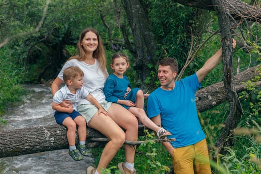 A joyful family is bonding together on a fallen tree by the flowing river in a beautifully lush green environment