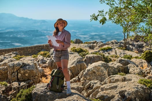 A woman in casual outdoor attire navigates a rocky terrain with a map. The image captures a sense of adventure and exploration, set against a breathtaking natural backdrop.