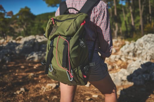 A person wearing a green backpack while hiking through a scenic forest trail. Outdoors, nature, adventure.