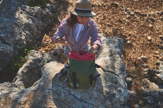 A young woman wears a hat and backpack as she explores a rocky landscape. Capturing the essence of adventure and discovery in nature, she appears ready for a hiking journey.