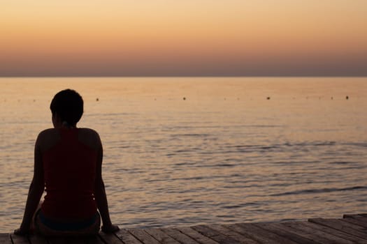 A person sitting on a pier looking at the sea during a beautiful sunrise over the horizon