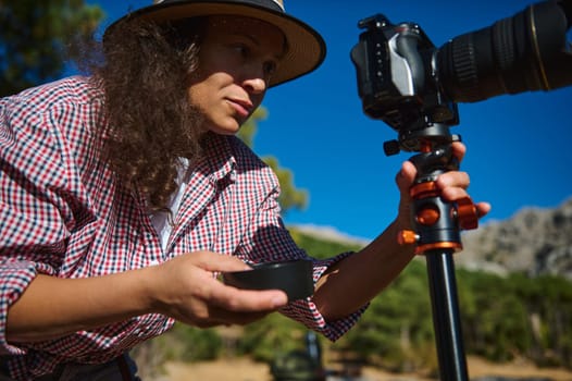 A focused photographer wearing a hat adjusts the camera on a tripod during an outdoor photography session, capturing the essence of nature with precision and dedication.