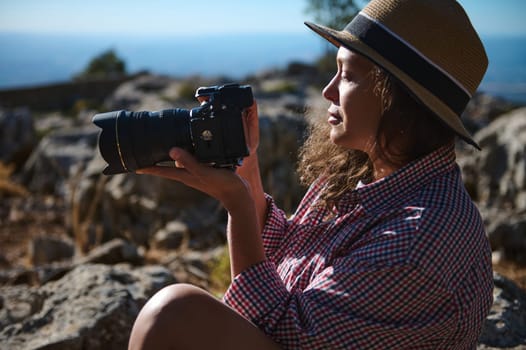 A woman, wearing a straw hat and plaid shirt, sits outdoors holding a camera. She is enjoying nature while photographing the rocky landscape. A sense of adventure and exploration.