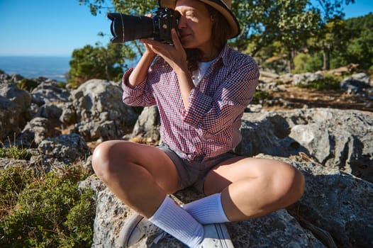 Outdoor adventure with woman capturing the beauty of nature in a rocky wilderness. Dressed casually, she wears a hat, shirt, and shorts, embodying travel and exploration vibes.