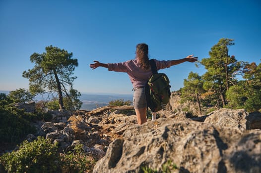 A person hiking on a rocky trail in nature, arms outstretched. Enjoying freedom, adventure, and peace in the wilderness under a clear blue sky.