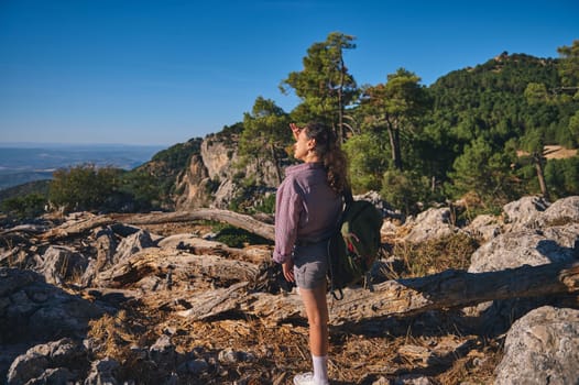 A young woman enjoys a sunny day hike, exploring the mountain terrain with lush greenery and expansive views, evoking a sense of adventure and freedom.