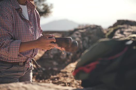 A person wearing a plaid shirt holds a wooden cup, enjoying coffee amidst scenic outdoor surroundings. The atmosphere conveys adventure, relaxation, and nature appreciation.