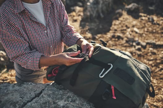 A woman adjusts the straps of her green backpack while hiking in a rocky outdoor setting, showcasing preparation and exploration.