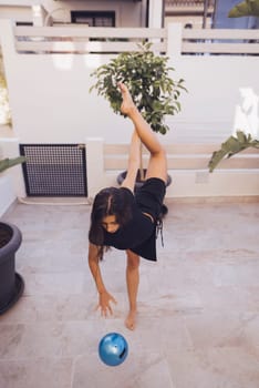 A young child demonstrating remarkable flexibility and balance while engaging joyfully with a ball in the outdoors