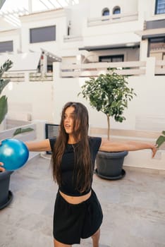A lively scene of a young woman joyfully posing with a blue ball, showing fun and relaxation in nature