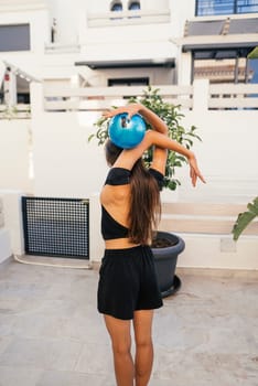 A woman performs an elegant yoga pose outdoors, showcasing strength and flexibility with a blue exercise ball.
