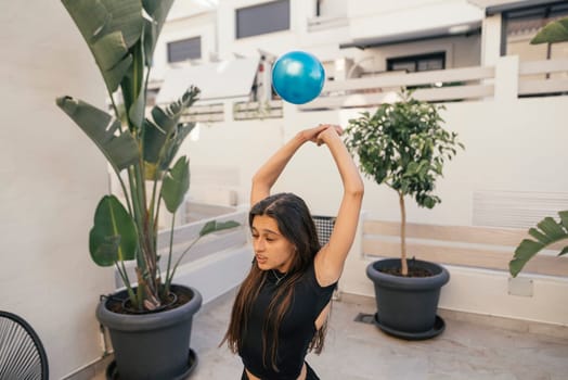 A woman is energetically performing a dynamic fitness routine with an exercise ball in a stylish, bright setting