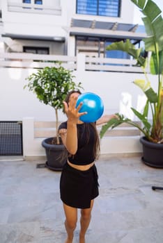 A cheerful woman enjoys a sunny day outdoors playing with a bright blue ball in a stylish and vibrant space