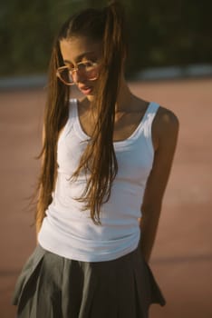 A playful young girl with long hair, wearing a white tank top and a skirt, exudes confidence and charm.