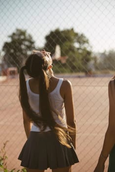 Two teenagers relax happily by a basketball court, enjoying sunlight and sharing a joyful moment outdoors
